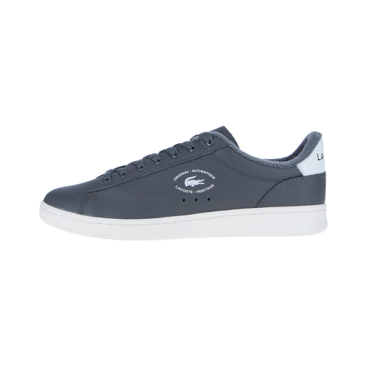Der LACOSTE CARNABY Set 224 2 SMA Sneaker in Dark Grey/Off White MN verfügt über eine weiße Sohle und Fersenlasche, Lacoste Logo und Text an der Seite und ist im Seitenprofil vor einem weißen Hintergrund dargestellt.