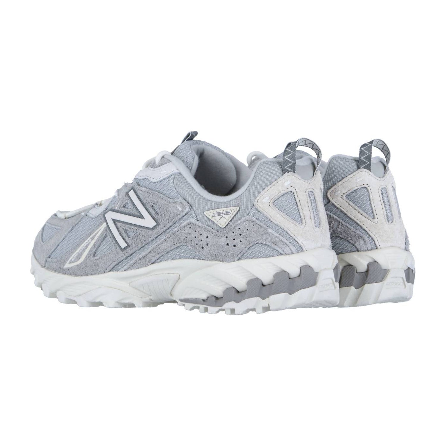 Ein Paar hellgraue New Balance ML610TV1 Trail-Sneaker mit weißer Sohle und Akzenten sowie ABZORB-Zwischensohlentechnologie sind von hinten und von der Seite auf weißem Hintergrund zu sehen.