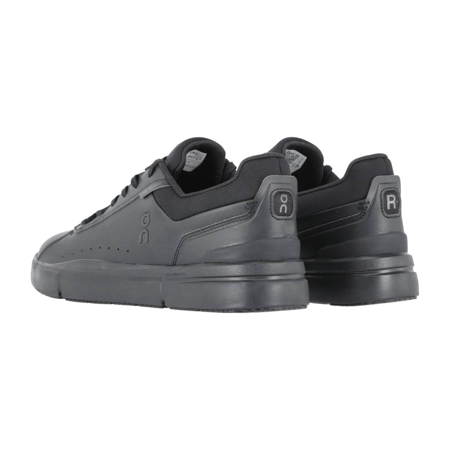 Ein Paar schwarze THE ROGER ADVANTAGE Sneakers von On mit ON- und RC-Logo an den Fersen, von hinten betrachtet, die das Low-Top-Design, die gepolsterten Sohlen und die Schweizer Performance-Technologie hervorheben.