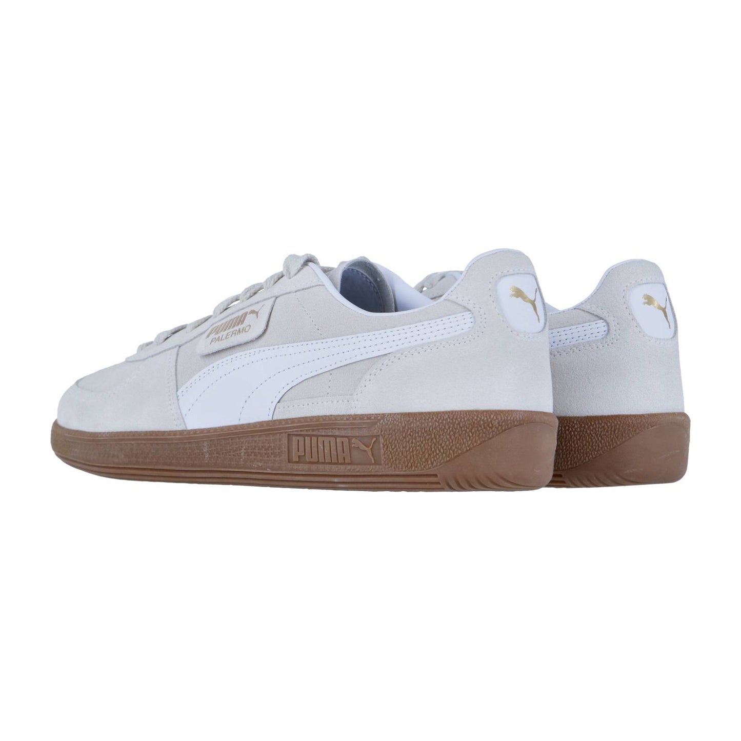 Die Puma Palermo Sneakers haben ein hellgraues Finish, weiße Seitenstreifen, goldene Logodetails und braune Gummisohlen. Von hinten und von der Seite vor einem weißen Hintergrund gezeigt, präsentieren sie einen Retro-Terrassen-Stil Look.