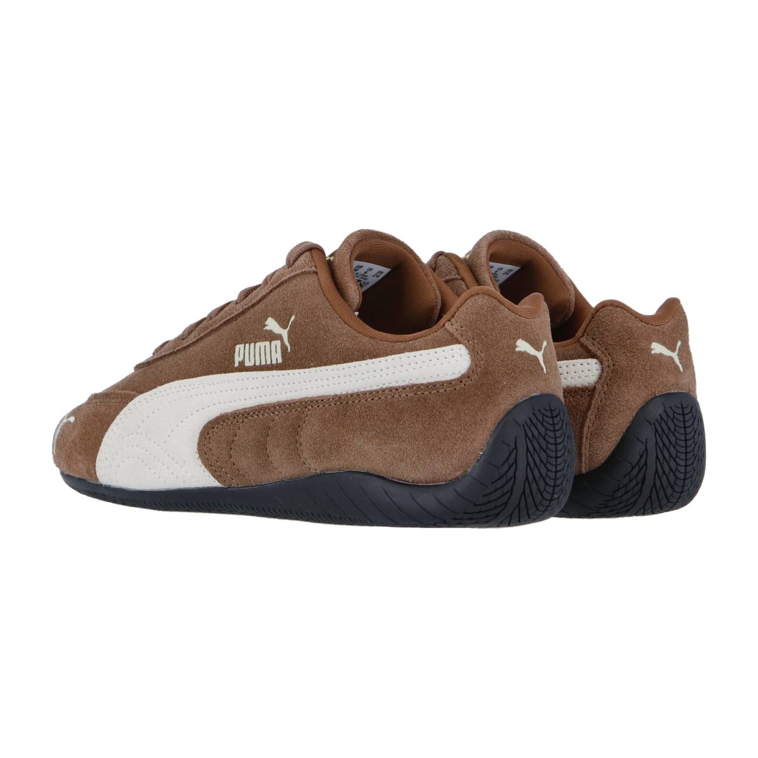 Ein Paar Puma Speedcat OG Sneakers aus braunem Wildleder mit weißen Logos und Seitenstreifen sowie schwarzer, strukturierter Sohle. Seite an Seite positioniert, fangen sie den echten Rennsport-Lifestyle ein, der mit der Marke Puma verbunden ist.