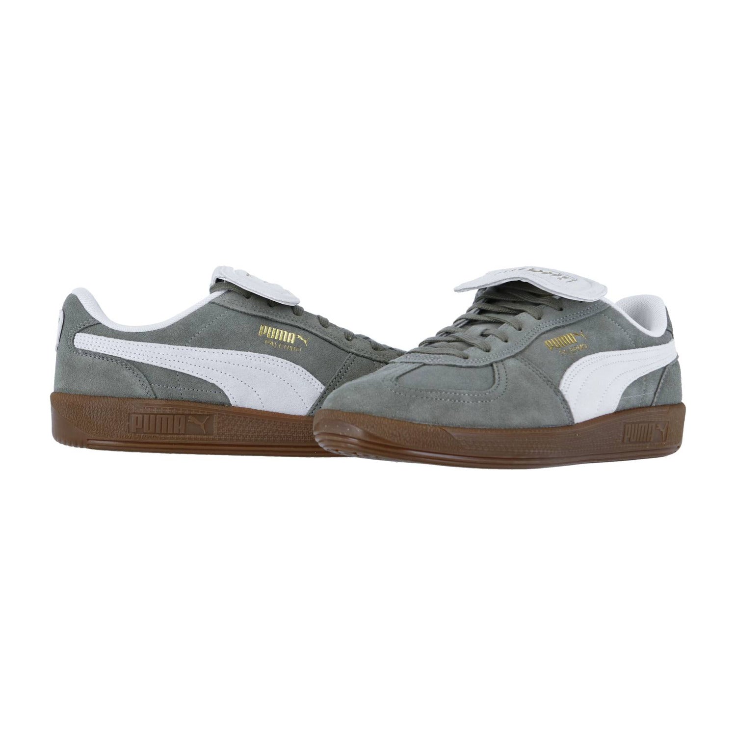 Ein Paar Puma Palermo PREMIUM Suede Sneakers in Grau mit weißen Akzenten und braunen Gummisohlen. Das goldene Puma-Logo hebt die Seite hervor, wobei ein Schuh aufrecht steht und der andere auf der Seite liegt.