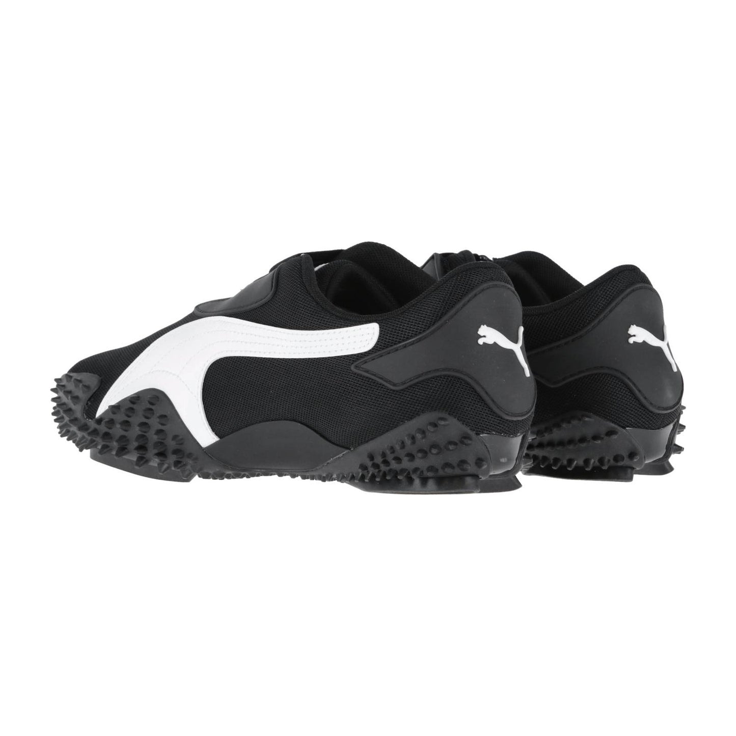 Ein Paar schwarze Puma Mostro OG Prime Turnschuhe mit weißen Puma Logos und Streifen, mit strukturierten Gummisohlen mit markanten Spikes für Grip, von hinten und von der Seite gezeigt.