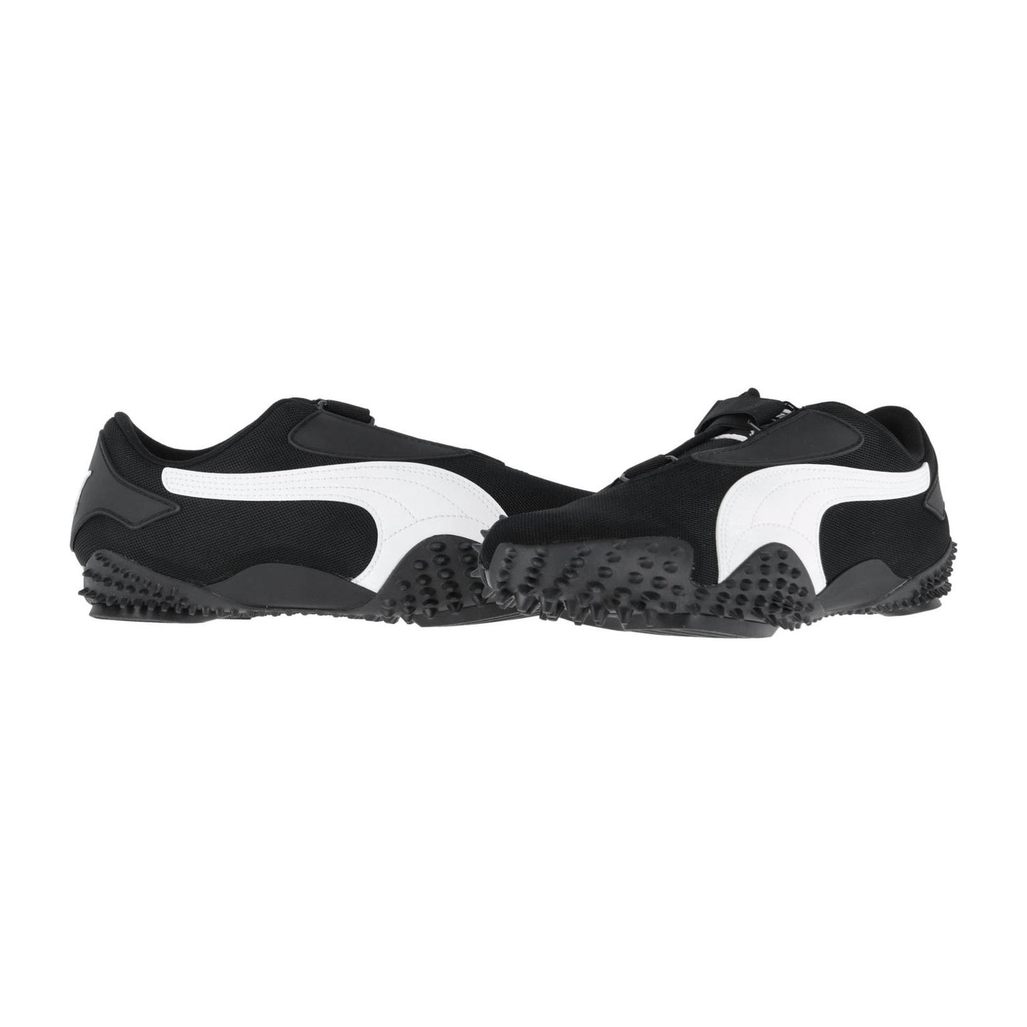 Ein Paar Puma Mostro OG Prime Sneakers in Schwarz, mit markanten weißen Seitenstreifen und strukturierten, gummierten Sohlen, stehen sich auf weißem Hintergrund gegenüber.