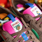 Nahaufnahme der braunen Rothaus Indoor Tannenzäpfle von Puma mit grünen Akzenten, rosa Zungen, blau und lila gestreiften Zuglaschen und einem einzigartigen Logo, das von den kultigen Tannenzäpfle Schwarzwälder Kultbier inspiriert ist.