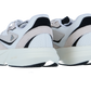 Zwei weiß-beigefarbene Adidas LIGHTBLAZE Sneaker mit schwarzen Akzenten wenden sich von der Kamera ab und präsentieren ihre Mesh-Textur, die klobigen Sohlen und die charakteristische LIGHTSTRIKE-Zwischensohle vor einem weißen Hintergrund.