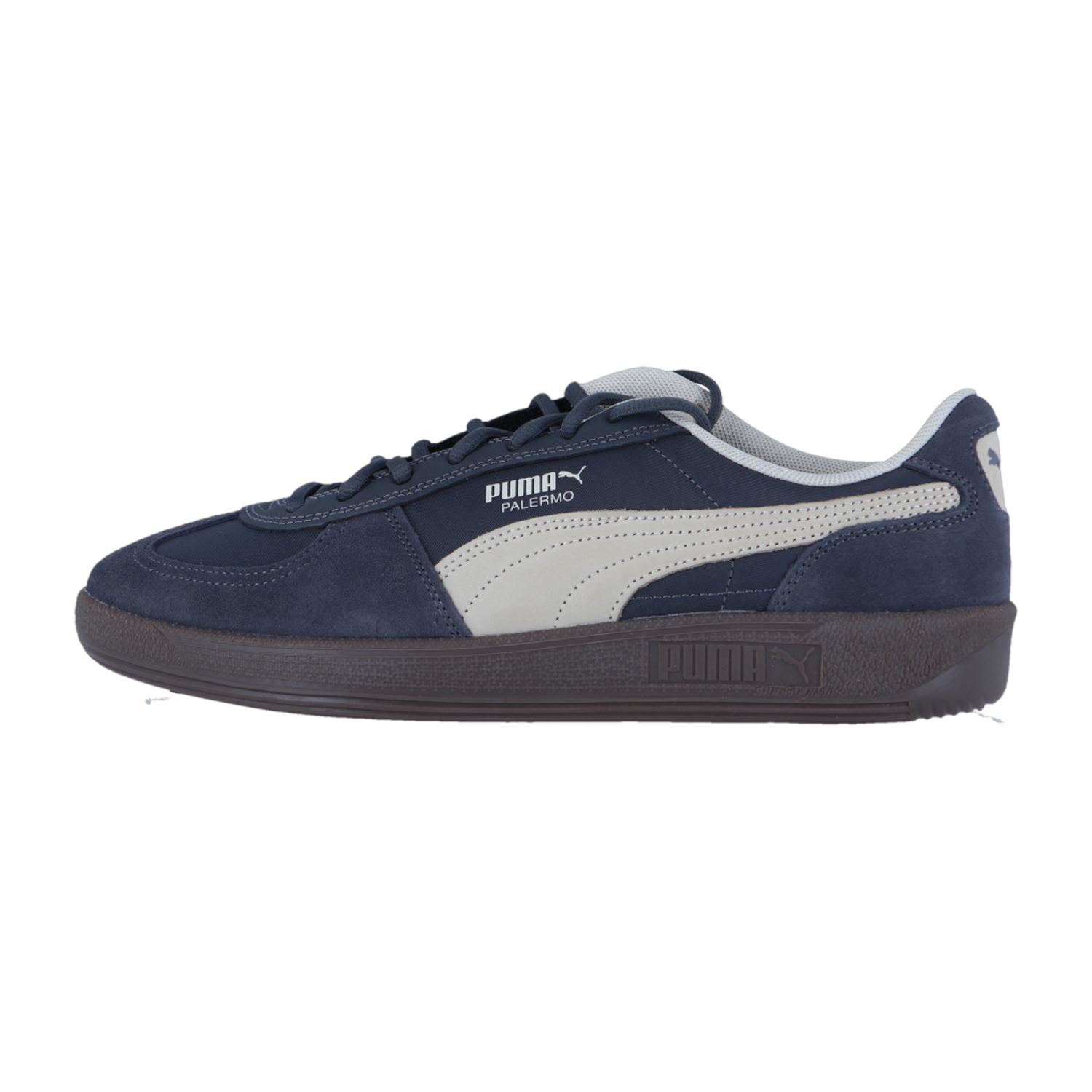 Der Puma Palermo Pop Retro-Sneaker hat ein marineblaues und weißes Wildleder-Obermaterial mit dem Puma-Logo und einer dunklen Sohle, die vor einem schlichten weißen Hintergrund steht.