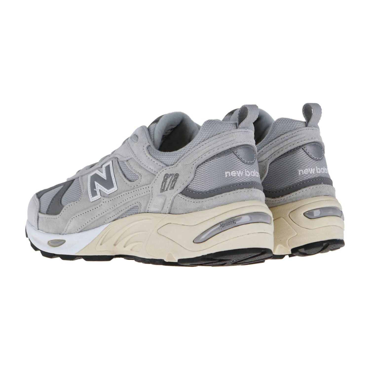 Ein Paar New Balance CM878V1 Sneakers in Grau mit ABZORB-Dämpfung, weißer und beiger Zwischensohle, schwarzer Laufsohle und dem N-Logo an der Seite, das in einem Winkel positioniert ist, um die hinteren und seitlichen Details zu zeigen.