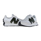 Ein Paar New Balance WS327V1 Turnschuhe mit weißem Obermaterial, dunkelgrünen N-Logos, grauen Wildlederakzenten und schwarzen strukturierten Sohlen; ein Schuh zeigt nach vorne, der andere ist leicht nach außen gewinkelt.