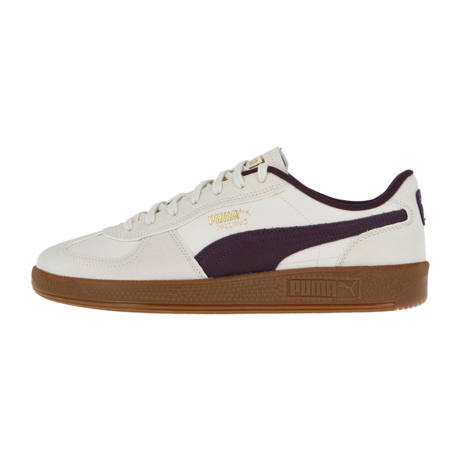 Der Puma Palermo Premium Sneaker wird von der linken Seite gezeigt. Er hat ein weißes Obermaterial, einen dunkelvioletten Streifen, ein goldenes Puma Branding und eine braune Gummisohle auf einem schlichten weißen Hintergrund.