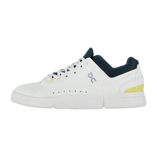 Der On THE ROGER ADVANTAGE ist ein weißer Low-Top-Sneaker mit dunkelblauem Futter, gelbem Fersenakzent, perforierten Seiten und einem grauen On-Logo. Er hat weiße Schnürsenkel und eine dicke weiße Sohle für klassischen Stil und Komfort.